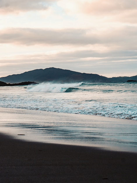 Vertical shot of the beautiful sea waves on the beach with the mountains