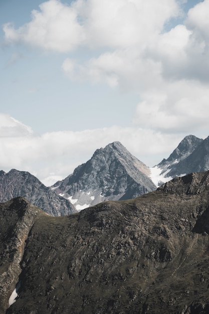 Vertical shot of beautiful snowy mountains under breathtaking clouds in light blue sky