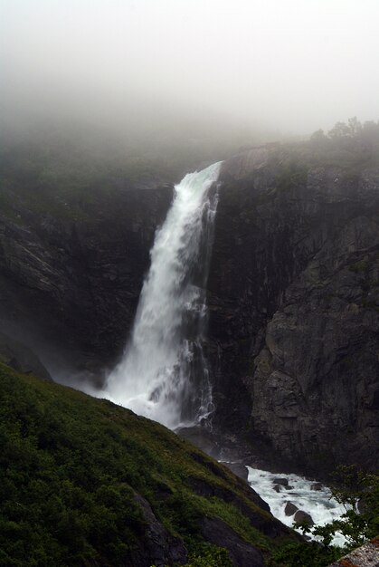 Vertical shot of a beautiful waterfall in the mountains enveloped with fog in Norway