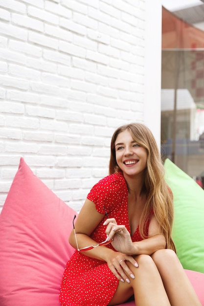 Free photo vertical shot of a beautiful woman having fun in an outdoor cafe, sitting on bean bag chair