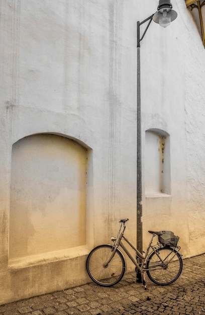 Free photo vertical shot of a bicycle parked next to a streetlamp in front of a white wall