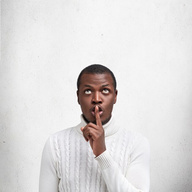 アフリカ系アメリカ人の黒人男性の垂直方向のショットは、人差し指を唇に置き、情報を秘密に保つように求めます