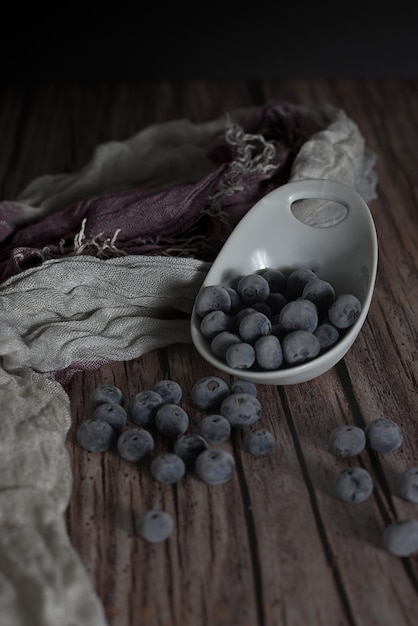 Vertical shot of black blueberries with a scarf behind it on a wooden table.