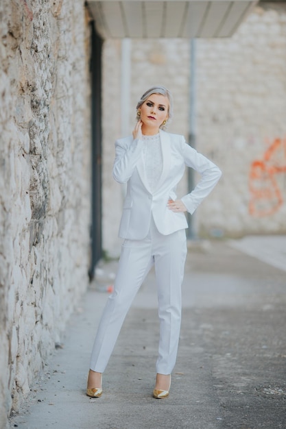 Vertical shot of a blonde female posing in an elegant white pantsuit