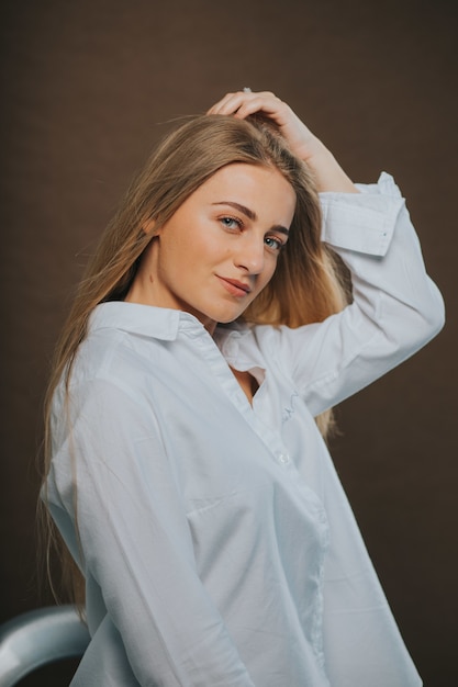 Vertical shot of an blonde female in a white shirt posing on brown