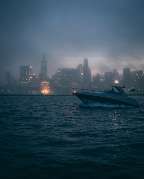 Vertical shot of a boat in the ocean with the silhouettes of high buildings