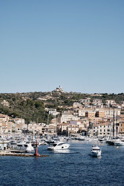 Vertical shot of boats on the water near buildings on the hill with a blue sky in the