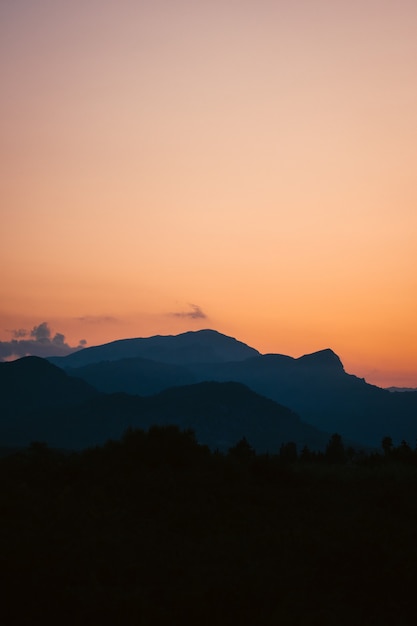 Vertical shot of a breathtaking sunset over the forest surrounded by mountains