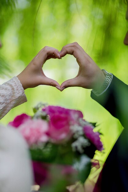 Vertical shot of a bride and a groom holding a heart with their hands