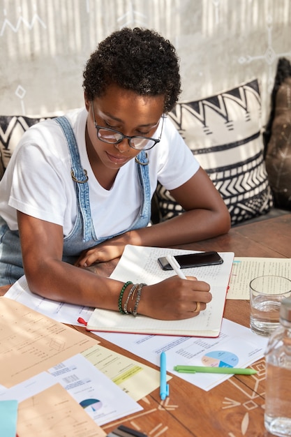 Free photo vertical shot of busy financial director analyzes information in papers, writes down in notebook