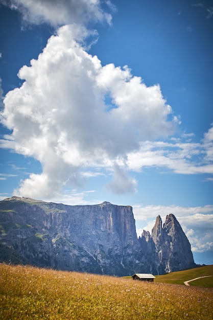 Vertical shot of a cabin in a grassy field surrounded by high rocky cliffs in Italy