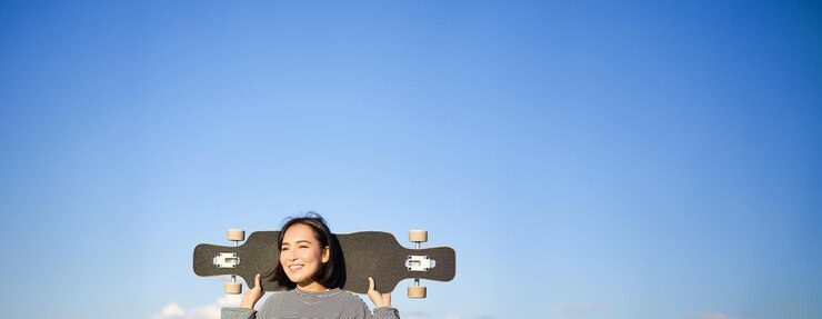 無料Photo ロングボードの若い女性スケート選手がクルーザーを握っている気のないアジアの女の子の垂直ショット