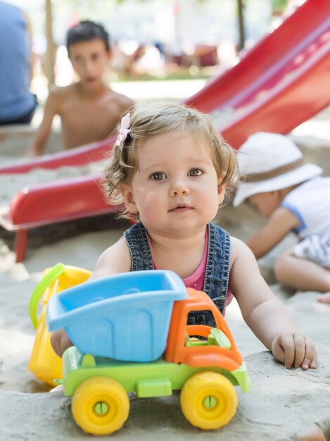 Vertical shot of Caucasian kid playing with toys on sandy playground