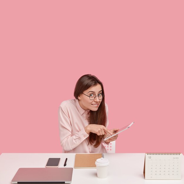 vertical shot of cheerful brunette young woman makes online booking ticket on touchpad, works as administrative manager