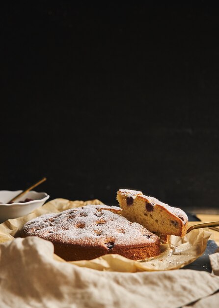 黒の側面に粉砂糖と材料が入ったチェリーケーキの垂直ショット