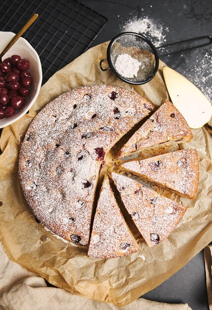 Vertical shot of a Cherry Cake with sugar powder and ingredients on the side on black