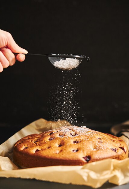 Foto gratuita colpo verticale di una torta di ciliegie con zucchero in polvere e ingredienti