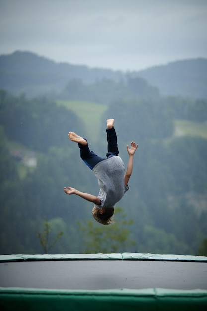 Free photo vertical shot of a child jumping on a trampoline with mountains