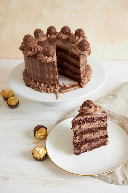 Вертикальный снимок шоколадного торта и кусочка на тарелке рядом с кусочками шоколада