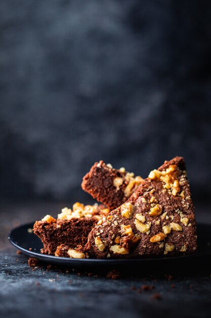 Vertical shot of a chocolate cake with walnuts in a black plate with a blurred