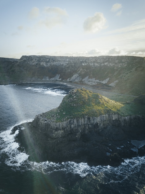 Free photo vertical shot of a cliff by the water under a clear sky with clouds