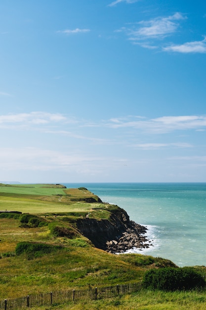 Vertical shot of cliff with a grassy field near the sea under a blue sky at daytime in  France