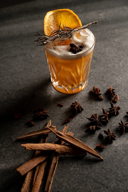 Vertical shot of a cocktail with an orange slice and dry herbs near a cinnamon sticks