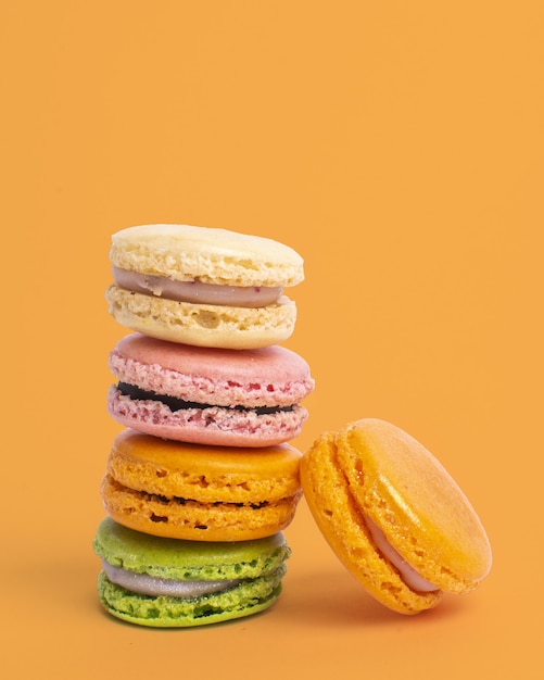 Vertical shot of colorful balancing macaroons against a yellow