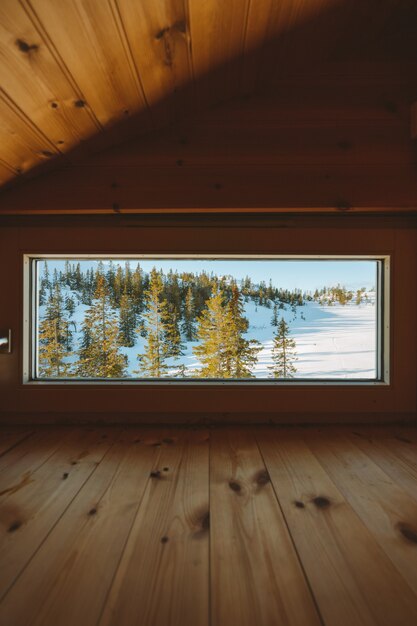 ノルウェーの雪に覆われた森の景色を望む窓のある居心地の良い屋根裏部屋の垂直ショット