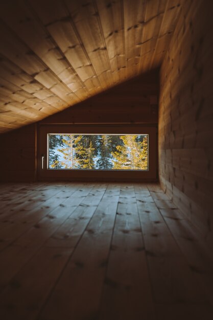 노르웨이의 눈으로 덮여 숲의 전망이있는 창문이있는 아늑한 다락방의 세로 샷