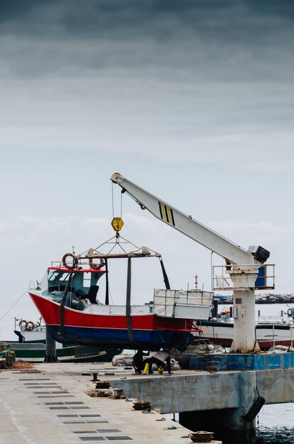 Vertical shot of a crane lifting a white boat on a pier