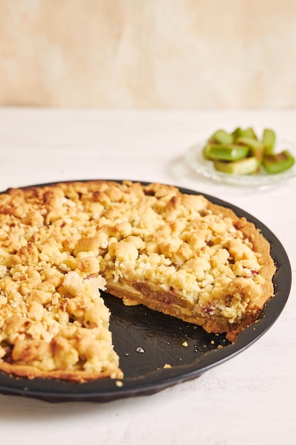 Vertical shot of a crispy Rhabarbar cake tart and some ingredients on a white table