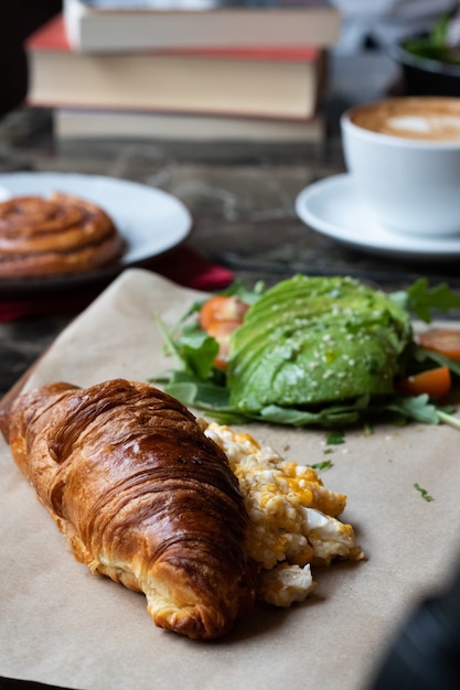 Vertical shot of a croissant with eggs and fresh avocadoes on a parchment paper