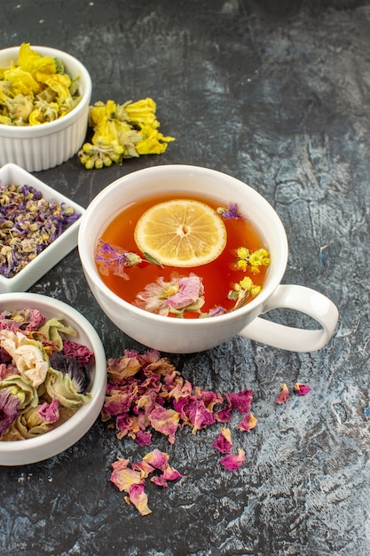 Vertical shot of a cup of herbal tea near bowls of dry flowers on grey background
