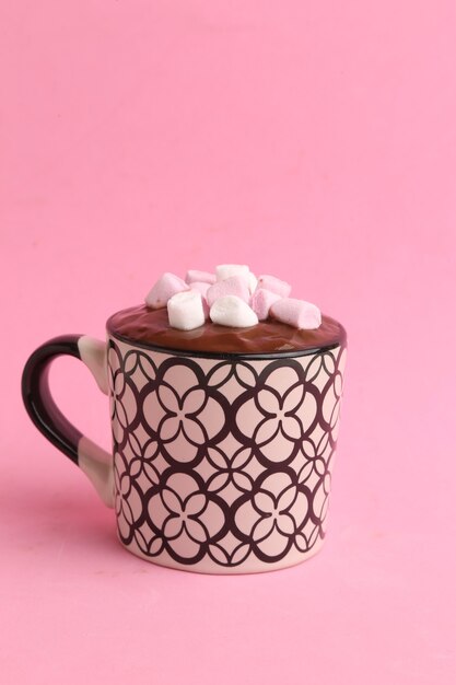 Vertical shot of a cup of hot chocolate with marshmallows isolated on a pink background