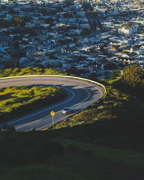 Vertical shot of a curvy road down the hill with buildings in the distance