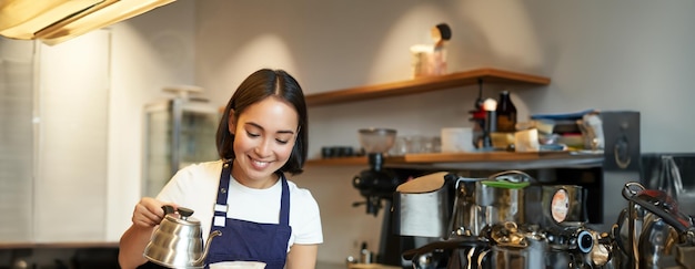 Vertical shot of cute asian girl barista student working in coffee shop pouring water in filter