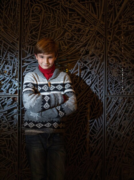 Free photo vertical shot of a cute boy with crossed hands standing in front of a wall