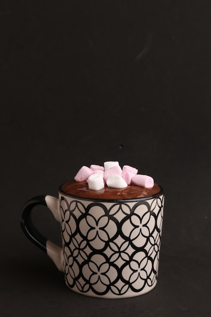 Colpo verticale della tazza decorativa con cioccolata calda e marshmallow su un nero