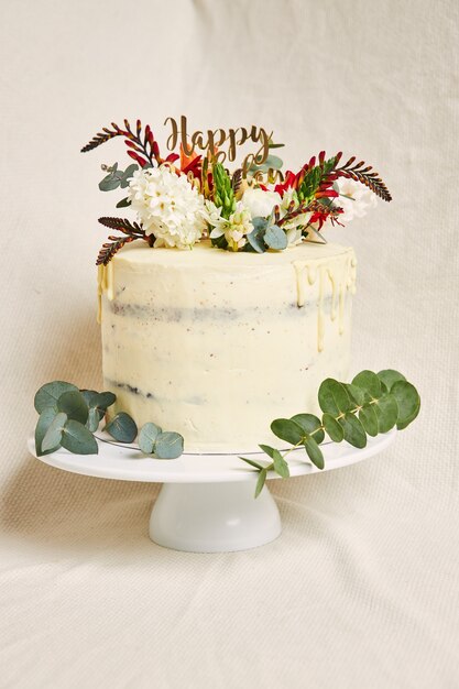 Vertical shot of a delicious birthday white cream flowers on the top cake with a drip on the side