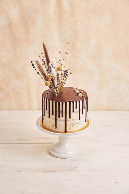 Vertical shot of delicious Boho cake with chocolate drip and flowers on top with golden decorations