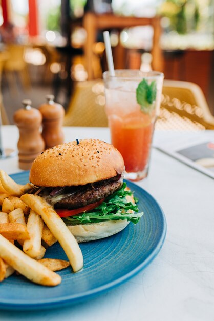 Vertical shot of a delicious burger and some french fries and a glass of cocktail on table