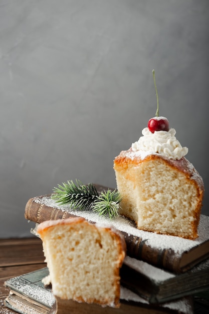Vertical shot of a delicious cake with cream, powdered sugar, and cherries on books