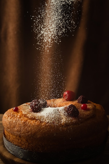 Vertical shot of a delicious cake with powdered sugar, red berries, strawberries, and blackberries