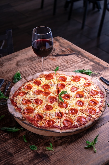 Vertical shot of a delicious cheesy pepperoni pizza with a glass of wine on a wooden table