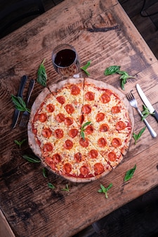 Vertical shot of a delicious cheesy pepperoni pizza with a glass of wine on a wooden table
