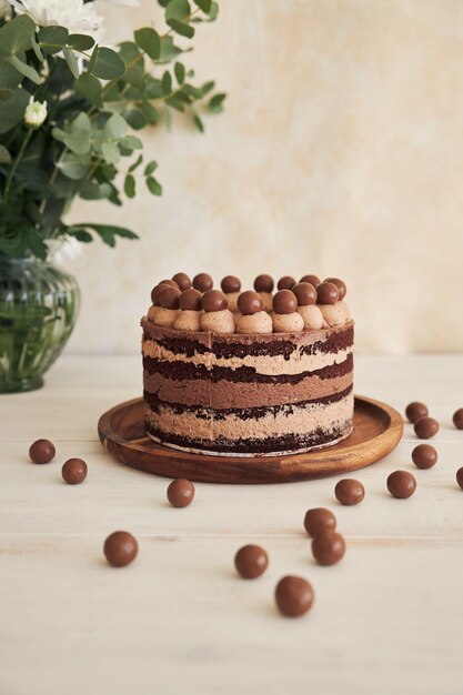 Vertical shot of a delicious chocolate naked cake with choco balls and cream on a white table