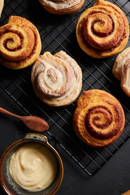 Vertical shot of delicious Cinnamon Rolls with a metal bowl of  White Glaze on a black table