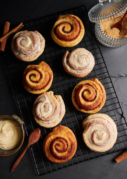 Vertical shot of delicious Cinnamon Rolls with a small bowl of White Glaze on a black table