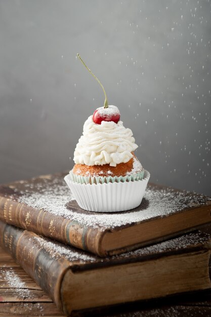 Vertical shot of a delicious cupcake with cream and cherry on top on books